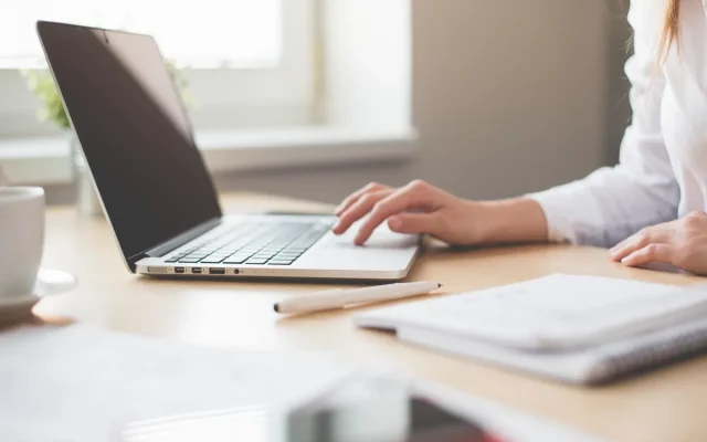 Seorang profesional muda sedang duduk di meja kerja dengan laptop di kantor yang terang