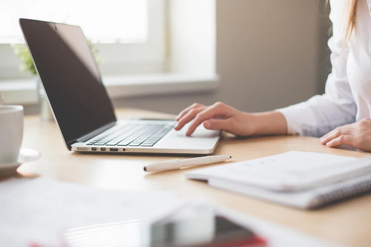 Seorang profesional muda sedang duduk di meja kerja dengan laptop di kantor yang terang