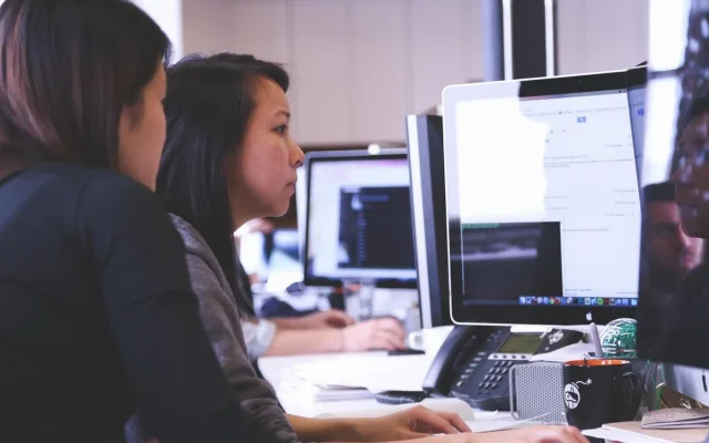 Seorang profesional muda sedang bekerja di depan laptop dengan latar belakang kantor modern yang cerah.