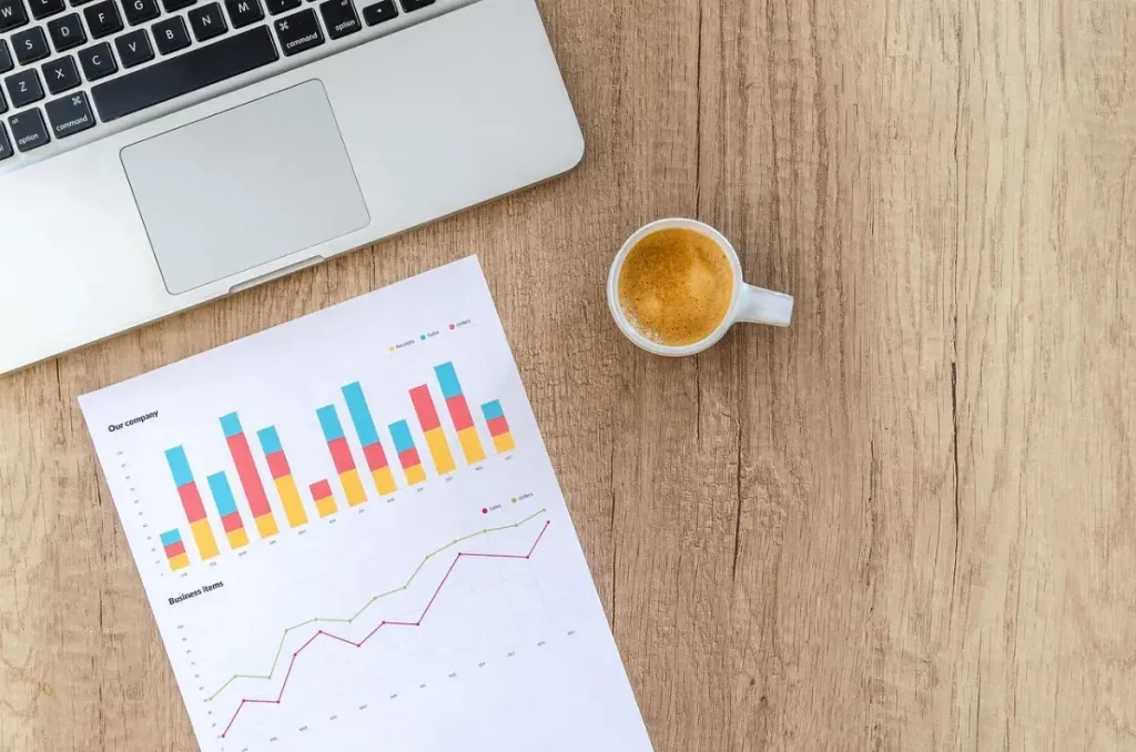 Seseorang sedang menganalisis grafik dan data di layar laptop dengan pencahayaan alami.