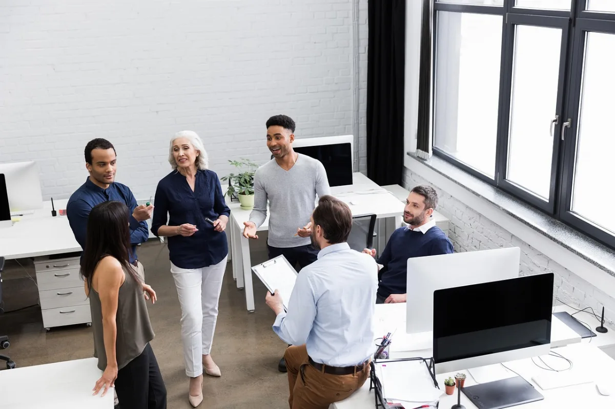 Seorang manajer baru sedang berdiskusi santai dengan anggota timnya di ruang kantor modern.
